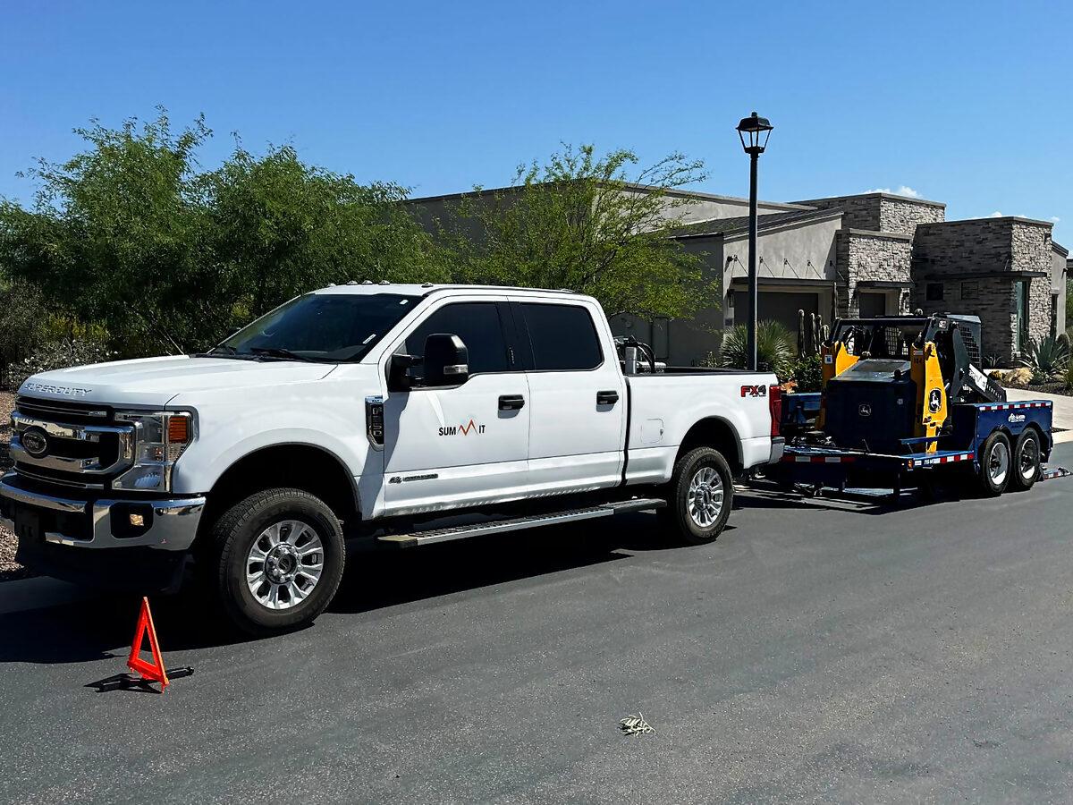 Summit Rentals pickup and trailer delivering a John Deere skid steer to a home in the Phoenix valley