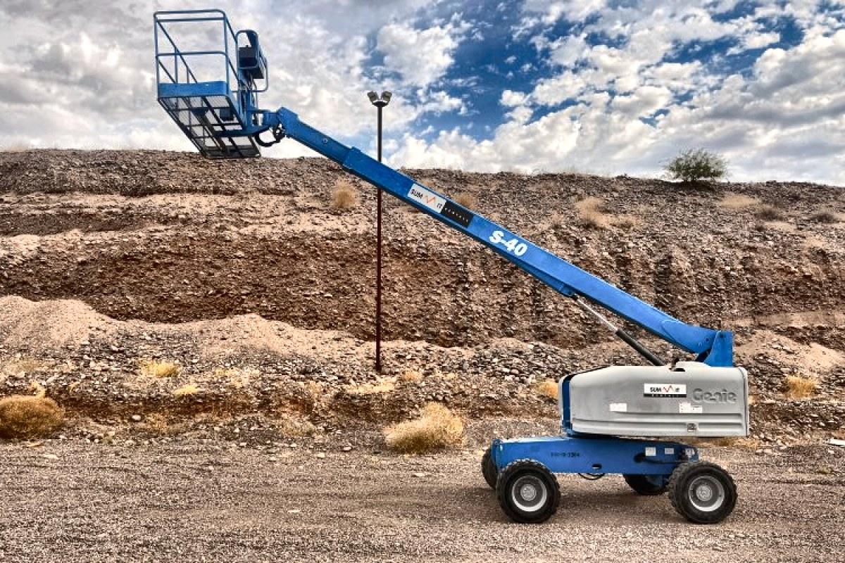 A Genie S-40 straight boom lift with the boom extended over rough desert ground