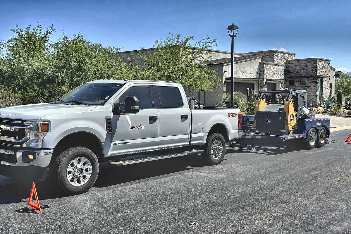 A Summit Rentals pickup and trailer delivering a skid steer to a Phoenix neighborhood